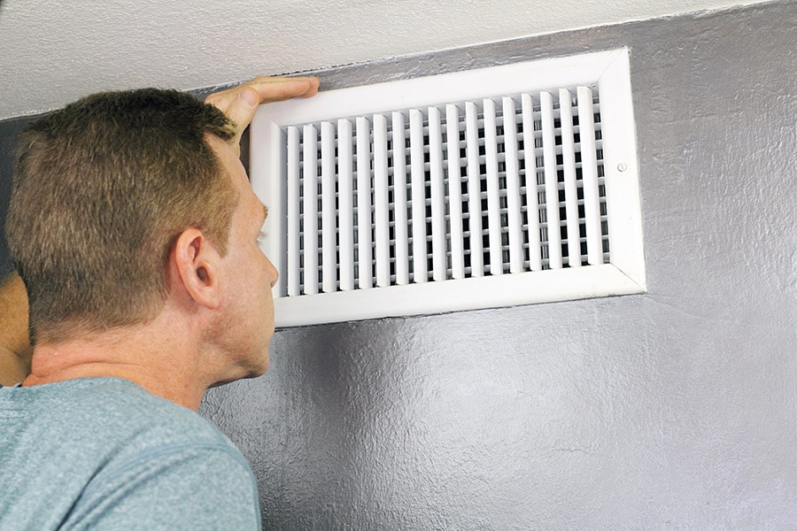 Homeowner inspects grille register of central HVAC system